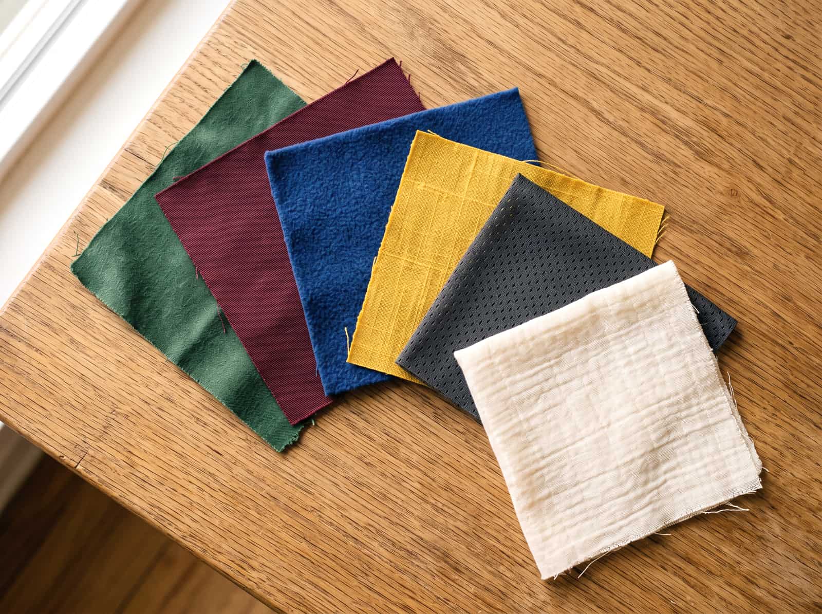 Fabric swatch squares fanned across a wooden surface in a range of colours.