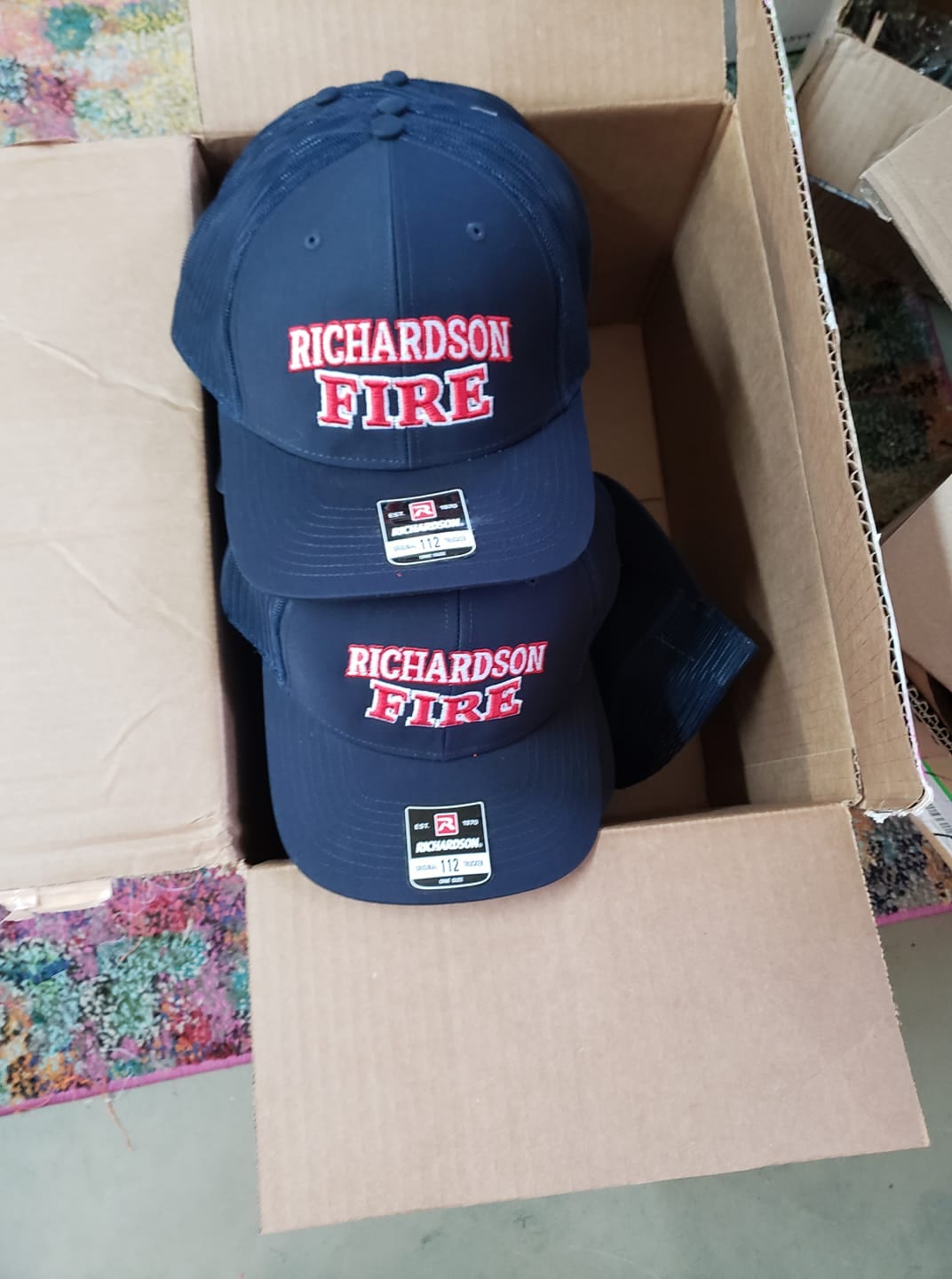 Navy Richardson Fire caps stacked in a box, each embroidered with the department mark.